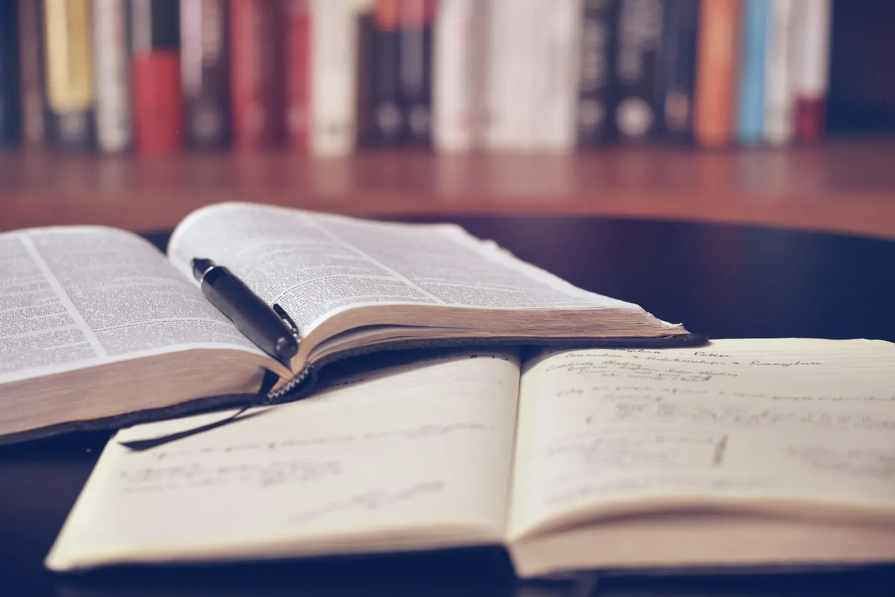 Открытая книга и конспект от руки на фоне книжных полок